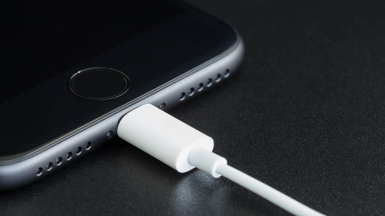 An iPhone with a charging cable plugged into it set against a black background