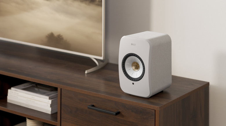 The KEF LSX II speaker sitting on a console next to a flatscreen TV