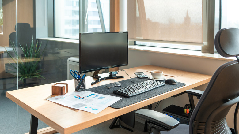 A desk setup for working from home including a monitor, keyboard, mouse, and other tools