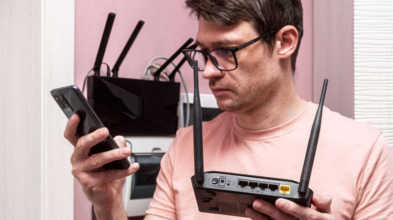 A man holding a Wi-Fi router in one hand and a phone in the other with a worried expression on his face