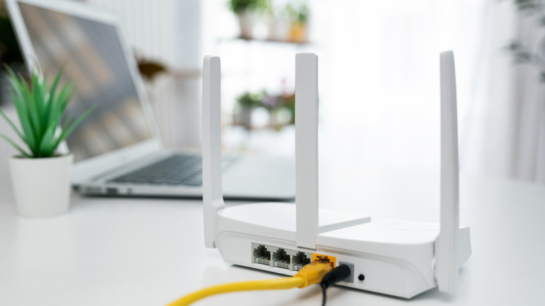 A sleek white internet router plugged in with a black power cable and a yellow Ethernet cable