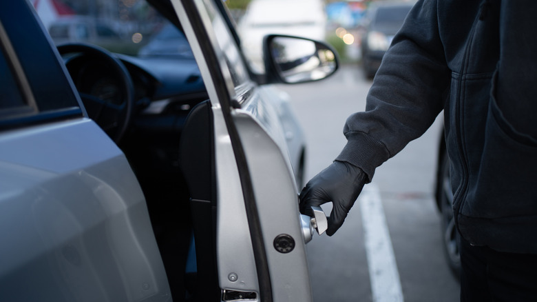 Gloved and hooded thief entering a vehicle by opening the door.