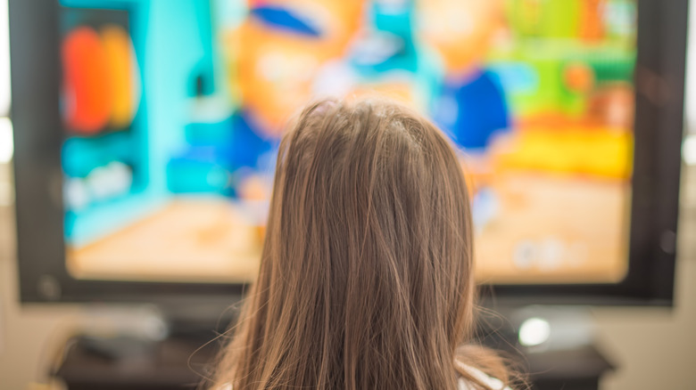 The back of a blond child's head as they watch TV, the television is highly blurred