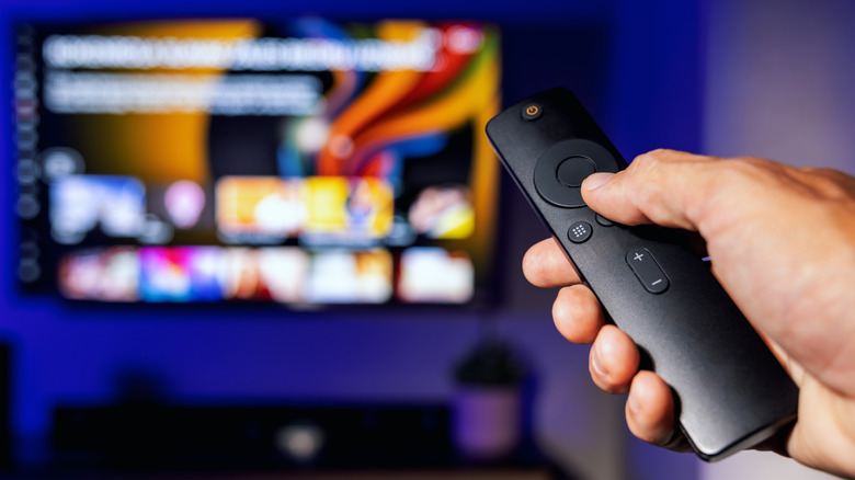 hand holding smart tv remote with a blurred TV screen visible in background
