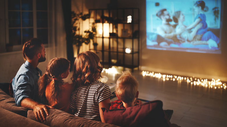 Family watching media content on a projector screen in a dimly lit room.