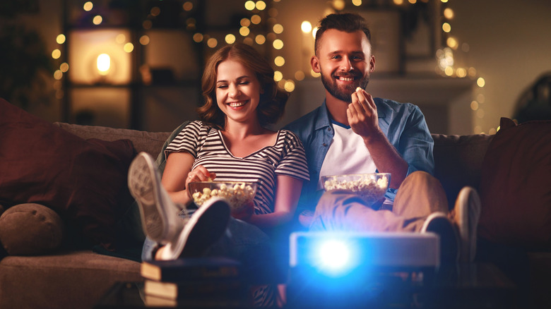 A couple enjoying entertainment via projector while eating popcorn