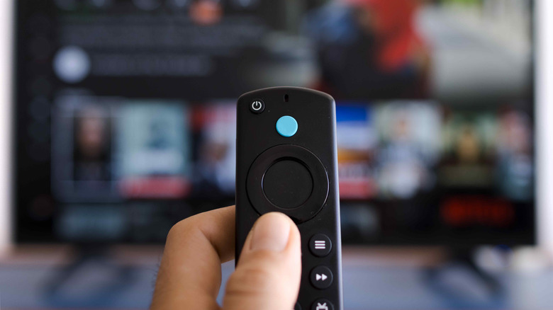 A person holding an Amazon Fire TV Stick remote in front of a TV screen.