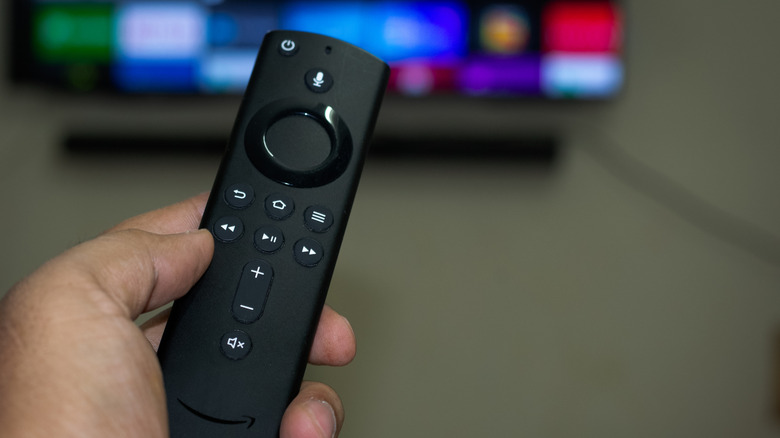 A person holding an Amazon Fire TV Stick remote in front of a TV.