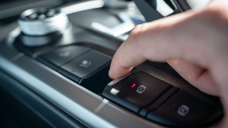 Close-up of a hand pressing the electronic parking brake on a car.
