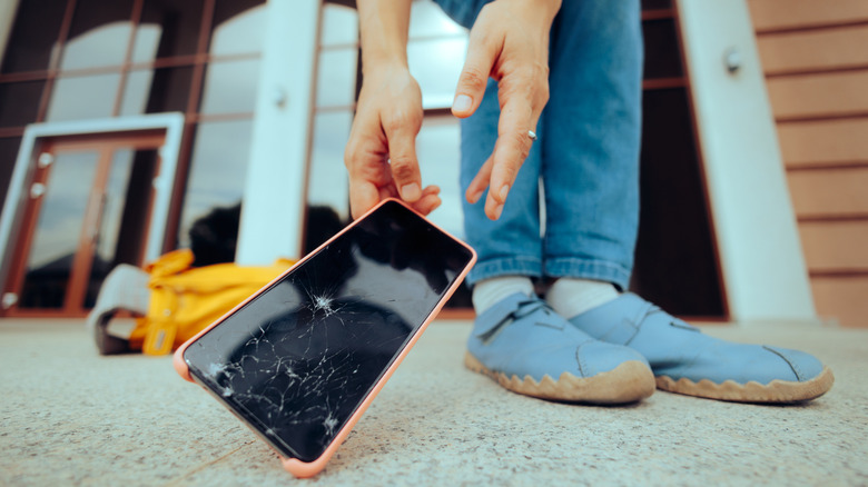 Person reaching for a smartphone with a cracked screen