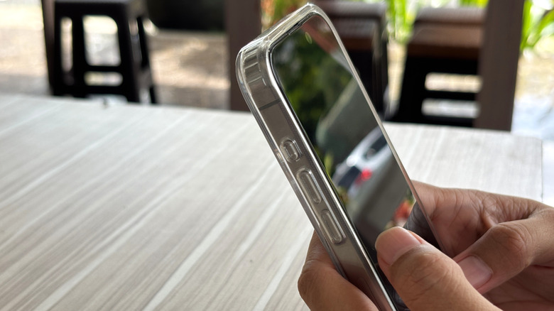 A person looking at their phone screen on a bright day, showing that it is darker from an angle.