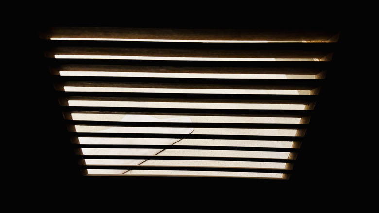 A set of blinds covering a window, partially open with some light coming through.