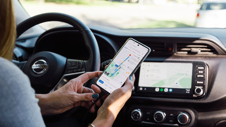 A driver checking Google Maps on their phone while it also displays on their dashboard.