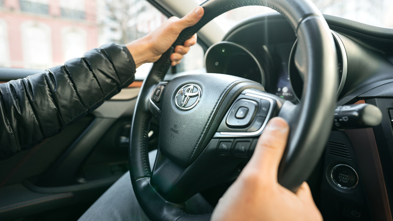 A person driving with the Toyota symbol on a car steering wheel