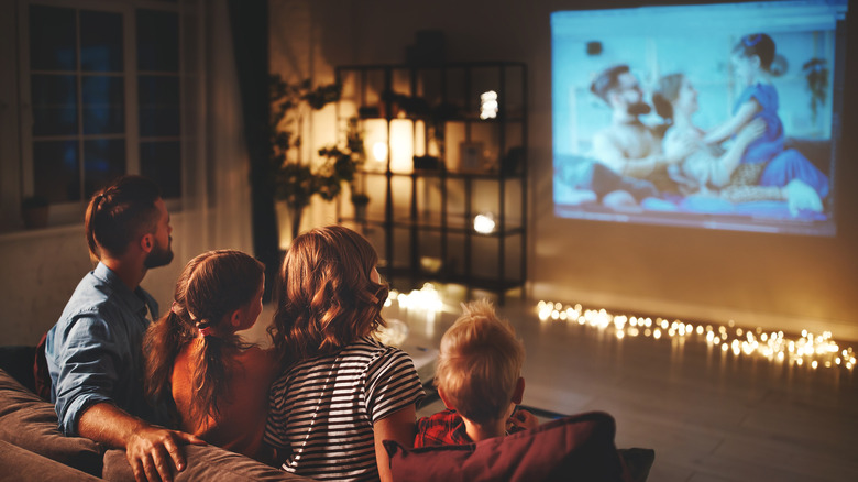 Family watching a movie with a projector in a dark living room