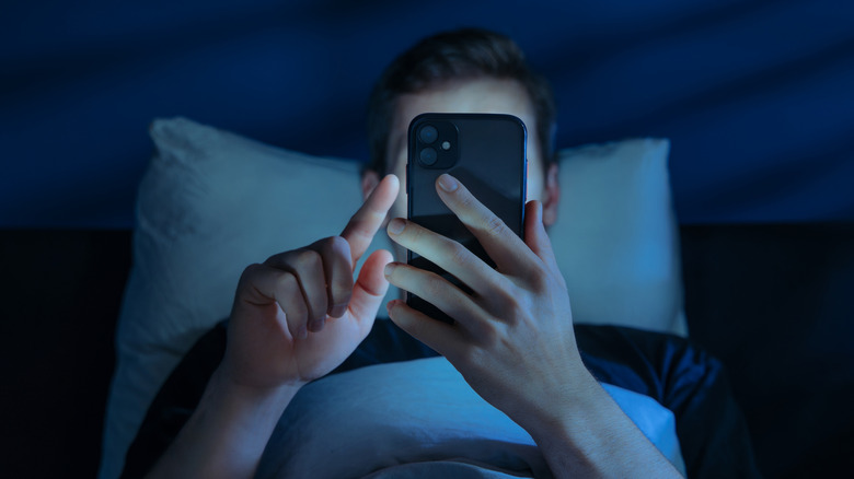 Someone holding a smartphone close to their face in bed.