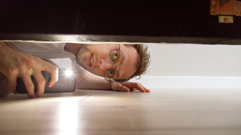 A person using a phone flashlight to look under the couch.