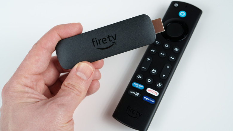 Someone holding an Amazon Fire TV stick next to the remote