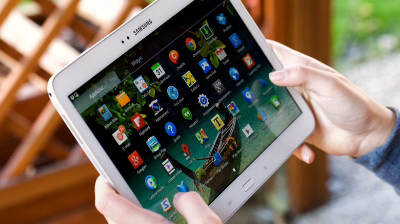 A person holding a Samsung tablet showing apps on the home screen