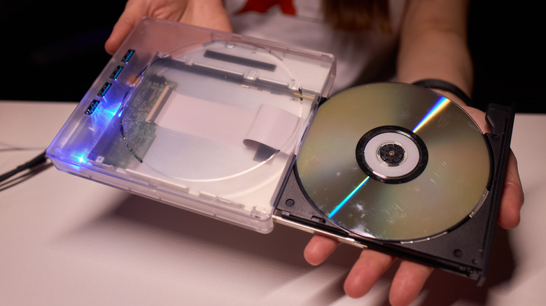 A person holding an external optical disc drive with a clear plastic enclosure and a disc being inserted