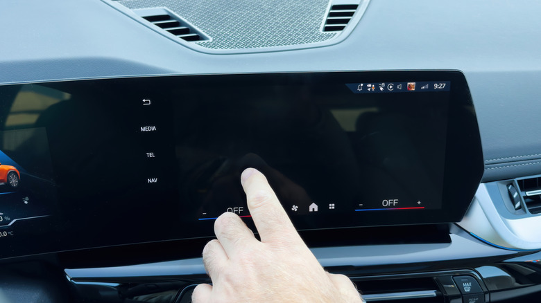 A person trying to interact with an unresponsive car touchscreen, which is partially black