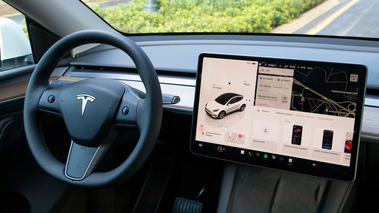 Interior of the Tesla Model Y, showing a steering wheel with the Tesla logo and a large touchscreen dashboard