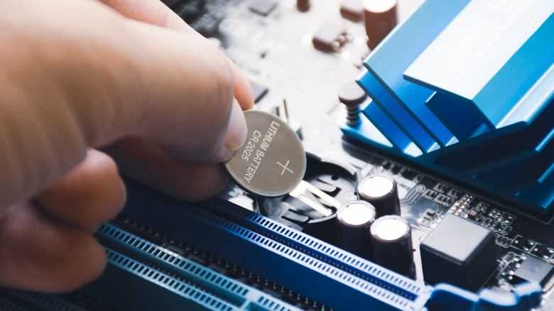 Someone installing a new CMOS battery into a motherboard slot.
