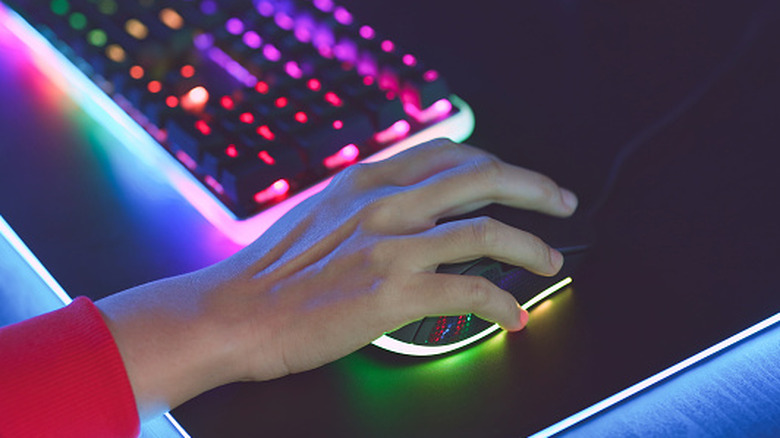 Hand resting on gaming mouse next to gaming keyboard.