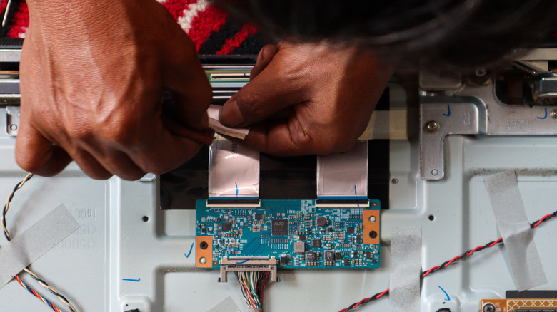 A pair of hands repairing components and circuit boards inside a TV