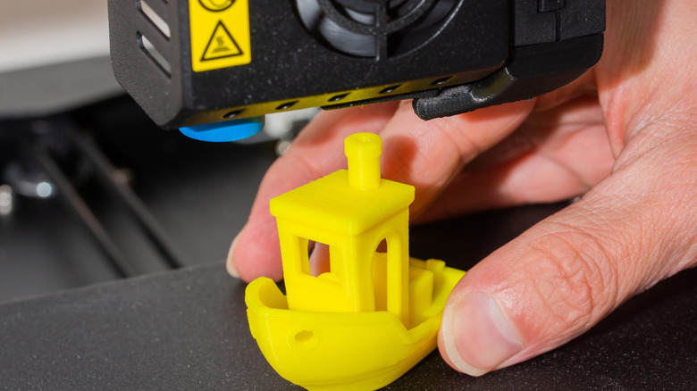 Man printing a yellow ship model with a 3D printer.