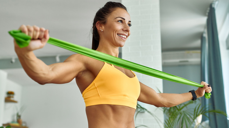 Woman working out with fitness strap on wrist using green resistance band.