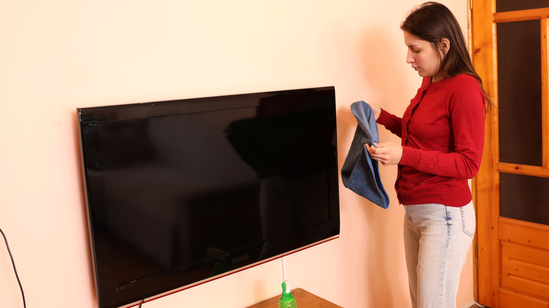 A girl cleaning the TV with a cloth