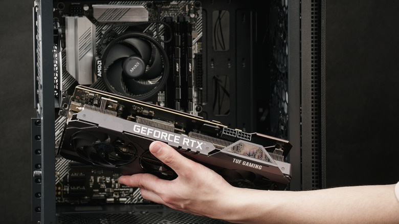 Person holding an NVIDIA GeForce RTX card near their PC
