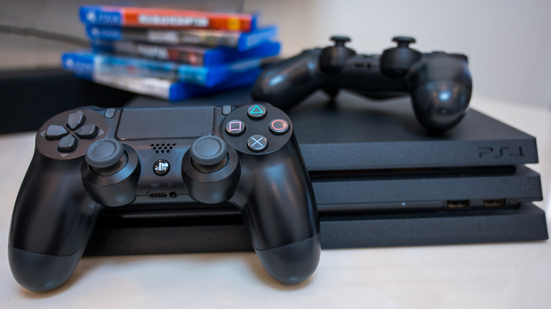 A PlayStation 4 Pro with two DualShock 4 controllers and a stack of games in the background