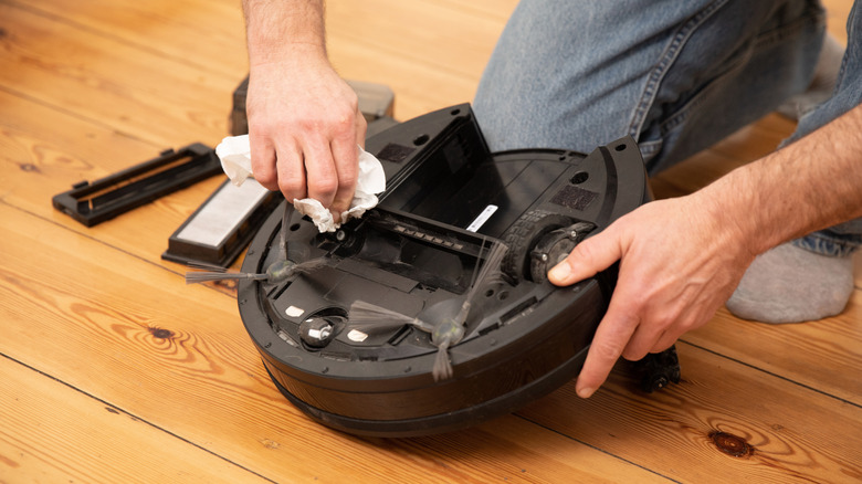 A person cleaning a robot vacuum cleaner.