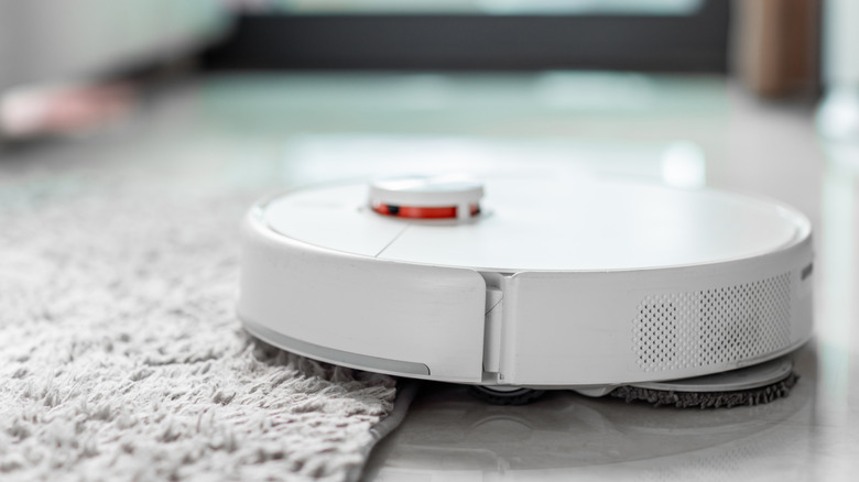 A white robot vacuum cleaner on a rug.