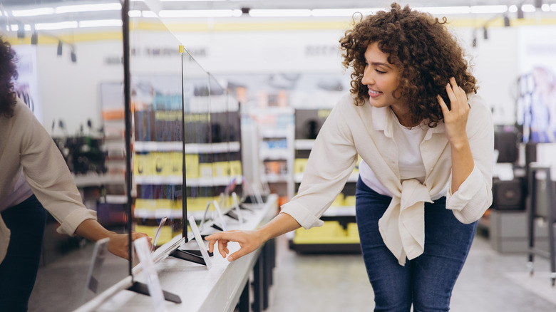 Woman inspecting a TV display in an electronics store.