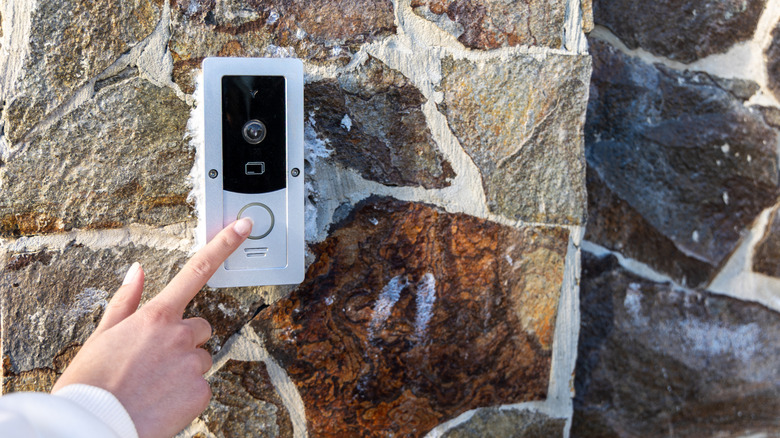 Hand pressing a video doorbell.