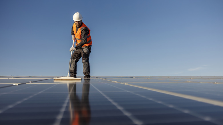 Someone cleaning solar panels on a large surface with many panels visible.