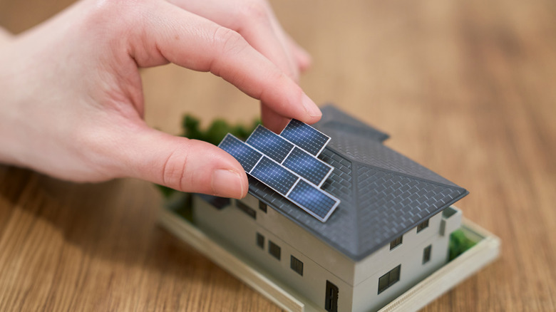 Someone's hand placing small solar panels on a model house.