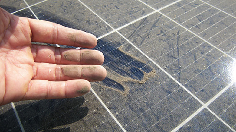 Close-up of a hand rubbing dust off a solar panel, creating a clean streak.