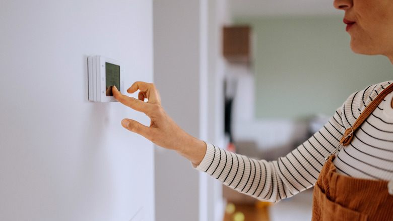 A woman interacts with a wall thermostat in a home.
