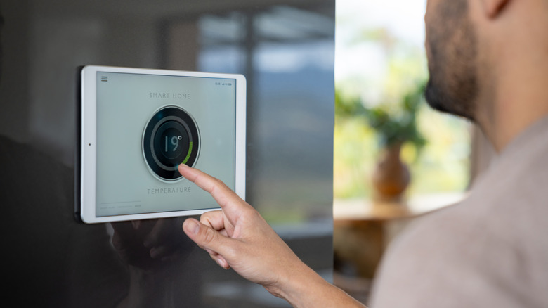 A man controlling a smart thermostat interface on a wall-mounted tablet.