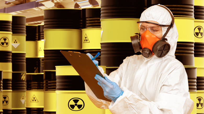 worker checking clipboard in front of several yellow and black barrels marked with radiation warning sign