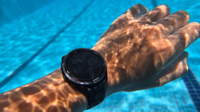 A hand wearing a Garmin smartwatch submerged in a swimming pool.