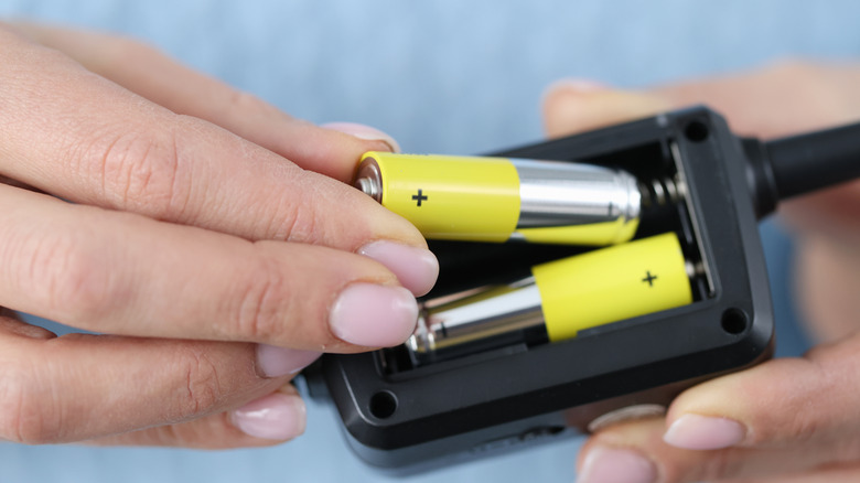Hands placing generic batteries into a battery port on a device.