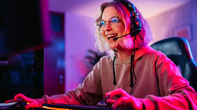 Young woman in front of a gaming PC with a headset on and smiling.