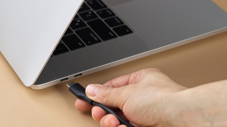 A hand plugging a USB cable into a laptop to charge it