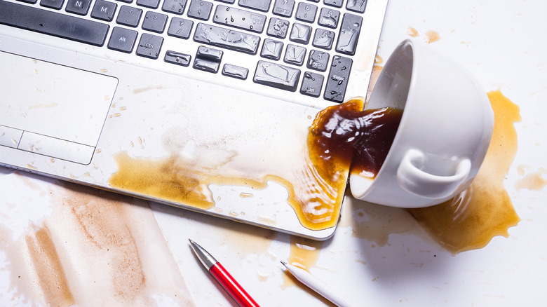 A cup of coffee spilling on a laptop keyboard.