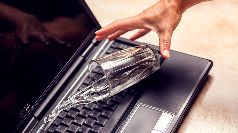 A glass of water spilling on a laptop keyboard.
